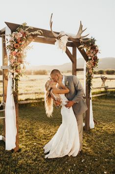 a bride and groom kissing under an arch decorated with antlers, flowers and greenery