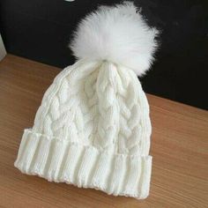 a white hat with a fur pom on the top sitting on a wooden table