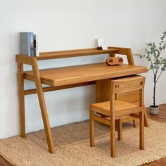 a wooden desk and chair in front of a white wall with a potted plant