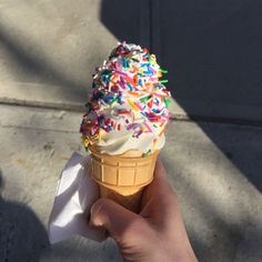 a hand holding an ice cream cone with sprinkles