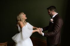 a bride and groom hold hands as they stand in front of a green painted wall