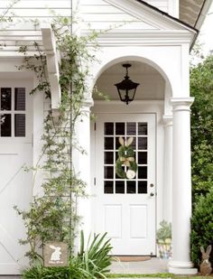 a white house with steps leading up to the front door and side entrance, surrounded by greenery