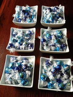 four white dishes filled with blue and silver candies on top of a wooden table