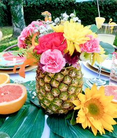 a pineapple with flowers and other fruit on a table in a backyard setting for an outdoor party