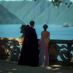 a man and woman standing next to each other in front of a body of water