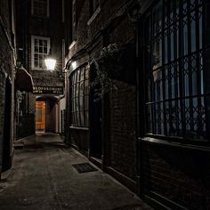 an alley way with brick buildings and windows at night, lit by street lamps on either side