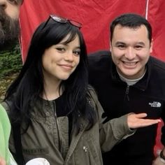 three people standing next to each other in front of a red tarp