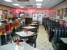 the interior of a restaurant with many tables and chairs, red neon lights hanging from the ceiling