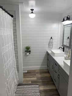 a bathroom with two sinks and a shower curtain in the corner is white shiplap