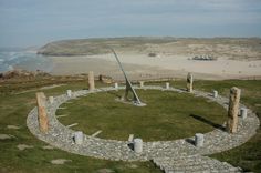 an aerial view of a circular stone structure in the middle of a grassy area with a beach in the background