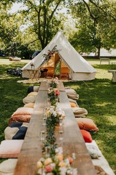 a long wooden table topped with lots of pillows next to a teepee tent in the grass