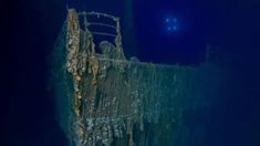 an old ship in the water with a blue light above it and a small boat below