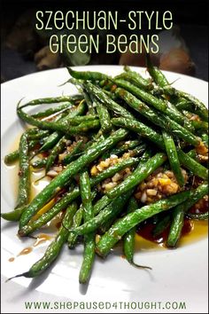 a white plate topped with green beans covered in sauce and seasoning on the side