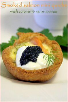 a small pastry with caviar and sour cream in it on a white plate