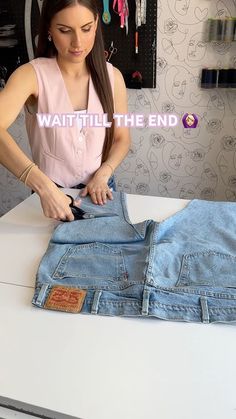 a woman in pink shirt and jeans cutting up some blue jean pants on top of a white counter