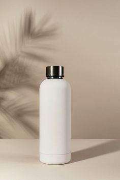 a white bottle sitting on top of a table next to a palm tree shadow wall