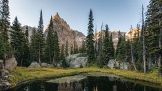 a lake surrounded by trees and rocks in the middle of a forest with mountains in the background