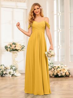 a woman in a long yellow dress standing on a wooden floor with flowers and greenery