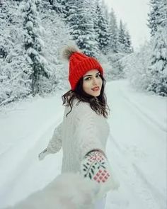 a woman walking down a snow covered road holding her hand out to the camera with trees in the background