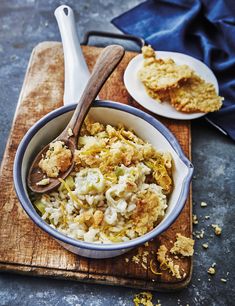 a wooden cutting board topped with a bowl of macaroni and cheese next to a plate of bread