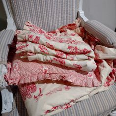 a pile of clothes sitting on top of a white chair next to a pillow and blanket