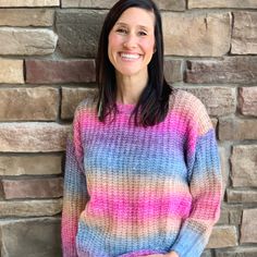 a woman standing in front of a brick wall wearing a multicolored knit sweater