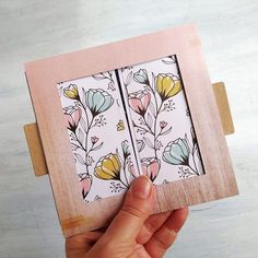 a hand holding up a small wooden box with flowers on the front and back sides