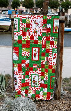 a red and green christmas quilt hanging on a wooden pole next to a body of water