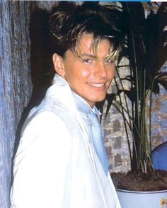 the young man is posing in front of a potted plant