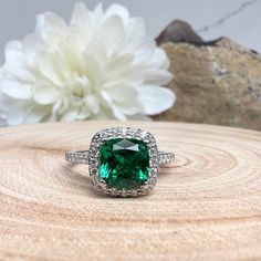 an emerald colored ring sitting on top of a piece of wood next to a flower