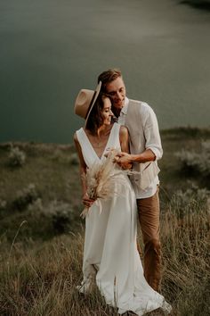 a man and woman standing on top of a grass covered field next to a body of water