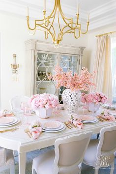 a dining room table with pink flowers in vases and plates on the place settings