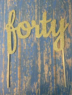 gold glitter name cake toppers on wooden sticks with blue background and wood planks