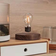 a light bulb sitting on top of a wooden table next to a glass vase with rocks in it