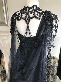 the back of a black dress with beading and pearls on it, sitting on a mannequin