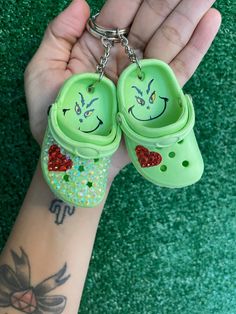 a person holding two green shoes with faces painted on them, and one has a red heart