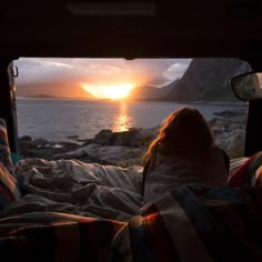 a woman is sitting in the back of a truck looking out at the ocean and mountains