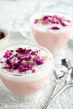 two desserts with purple flowers in them on a white tablecloth next to spoons