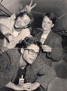 three people posing for the camera with one holding up his hand and two wearing glasses