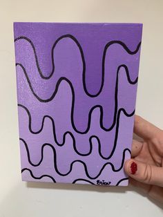 a hand holding up a purple and black painting on a white surface with wavy lines