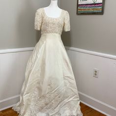 a white wedding dress on display in a room with wood flooring and wall hangings