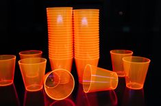 an assortment of neon colored plastic cups on a black table with red light reflecting off them