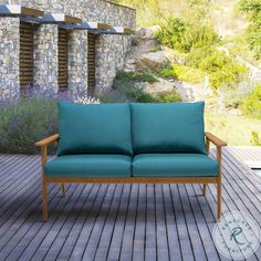 a blue couch sitting on top of a wooden floor next to a stone wall and purple flowers