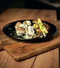 a black plate topped with meatballs and potatoes on top of a wooden cutting board