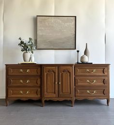 two vases are sitting on top of an old wooden dresser next to a painting