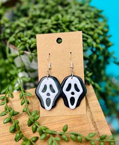 two black and white earrings on top of a wooden table next to green plants in front of a blue background