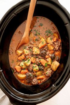 a wooden spoon is in a slow cooker filled with meat and potatoes, garnished with parsley