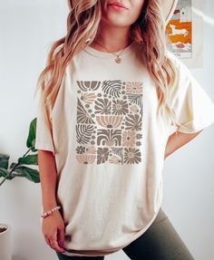 "Retro Boho Wildflowers Ivory Comfort Colors Shirt, Nature Botanical Floral Tee, Cottagecore Wild Flower Neutral Tone T-Shirt, Gift For Her PLEASE SIZE UP FOR AN OVERSIZED FIT If you are looking for an oversized \"T-shirt Dress\" look, we recommend sizing up 2 sizes. Comfort Colors introduces its garment-dyed t-shirt; a fully customizable tee made 100% with ring-spun cotton.  The soft-washed, garment-dyed fabric brings extra coziness to your wardrobe while the relaxed fit makes it an excellent daily choice. The double-needle stitching throughout the tee makes it highly durable while the lack of side-seams helps the shirt retain its tubular shape. .: 100% ring-spun cotton .: Medium fabric (6.1 oz/yd² (206.8 g/m .: Relaxed fit .: Sewn-in twill label" Beige Short Sleeve Top With Graphic Print, Beige Printed Cotton Tops, Printed Beige Cotton Tops, Beige Summer Top With Screen Print, Beige Relaxed Fit Top With Graphic Print, Beige Printed Cotton Shirt, Beige Cotton Printed Shirt, Beige Printed Shirt With Relaxed Fit, Cream Tops With Screen Print For Spring