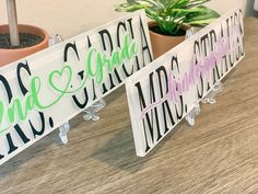 two signs that are sitting on top of a wooden table next to a potted plant