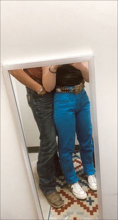 two people standing in front of a mirror with their arms around each other's waist